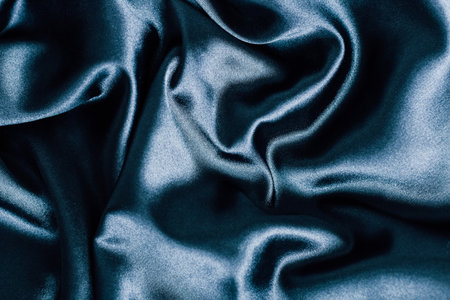 This deep blue satin fabric displays smooth glossy surfaces and gentle folds. Its rich color and texture create a luxurious appearance perfect for fashion or interior design projects.の写真素材