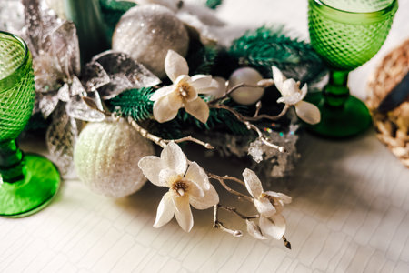 A beautiful holiday table setting showcases green glass cups alongside white flowers and decorative ornaments. The arrangement features winter greenery creating a festive and inviting atmosphere.の写真素材