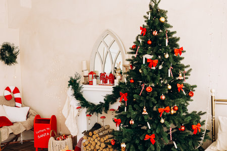 A cozy room features a beautifully decorated Christmas tree adorned with red bows and ornaments. Nearby a fireplace is decorated with festive garlands and a mailbox for letters to Santa.の写真素材