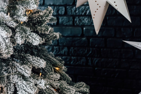 Decorations fill a warm space with a snowy Christmas tree adorned with lights and ornaments. A dark brick wall enhances the holiday atmosphere creating a festive and inviting scene.の写真素材
