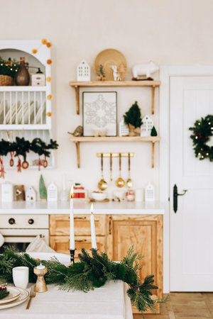 Warm kitchen set for the holiday season featuring a beautiful table decorated with greenery and candles. The shelves showcase charming holiday decor enhancing the cozy atmosphere.の写真素材