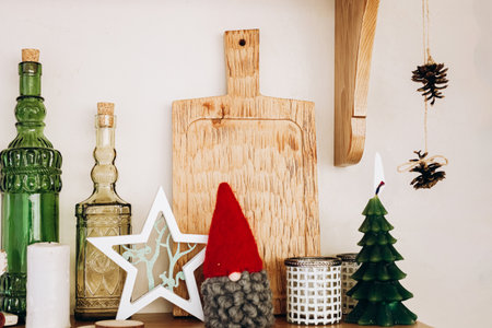 A warm and inviting shelf displays a wooden cutting board festive gnome small green tree and decorative glass bottles.の写真素材