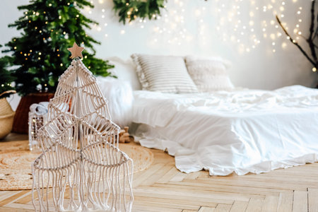 A cozy bedroom is decorated for the holidays with a unique macrame Christmas tree. Soft lights illuminate the space and a traditional tree stands nearby creating a warm festive atmosphere.の写真素材