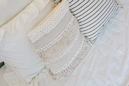 A warm and inviting bedroom features soft fluffy pillows along with a textured cushion on a light...
