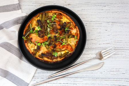 A beautifully arranged savory casserole sits on a black plate. Garnished with fresh herbs it features layers of vegetables and meat. A cloth napkin and cutlery complete the setting.の写真素材
