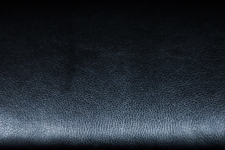 This scene features a close up view of black leather with a fine texture. The surface displays a smooth finish and a subtle sheen highlighting the quality of the material.の写真素材