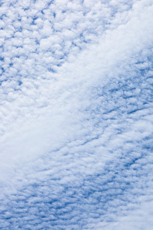 Cotton like clouds drift elegantly in the bright blue sky during a warm afternoon creating a peaceful and serene atmosphere. Sunlight illuminates the clouds enhancing their fluffy appearance.の写真素材