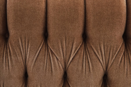 A tufted fabric backrest in a soft brown color showcases a plush texture. The folds create a...