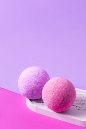 Two round bath bombs one purple and one pink are placed on a white tray. The background features soft pastel colors in purple and pink creating a calm and relaxing atmosphere.の写真素材