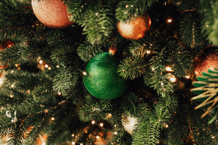 Bright green and gold ornaments hang from lush green branches of a Christmas tree. Twinkling lights create a warm holiday ambiance inviting feelings of joy and celebration during the festive season.の写真素材