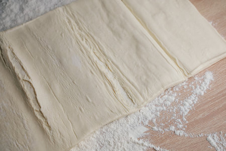 Soft layers of pastry dough are spread out on a wooden countertop sprinkled with flour. The kitchen is bright and cozy perfect for baking delicious treats.の写真素材