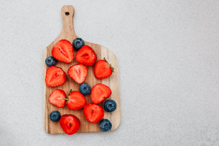 Bright red sliced strawberries and fresh blueberries are artfully arranged on a wooden cutting board. This vibrant display is perfect for a healthy snack or summer dessert.の写真素材