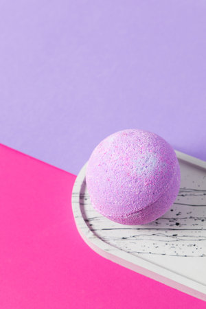 A round lavender bath bomb rests on a patterned tray against a backdrop of pink and purple hues. It adds a touch of color and tranquility perfect for a self care routine.の写真素材