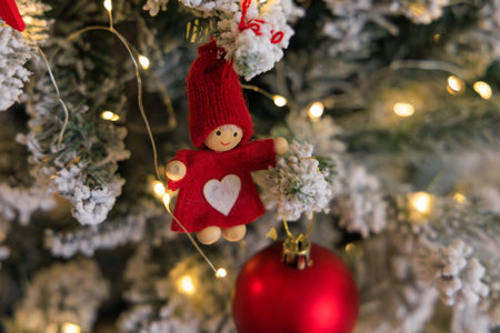 A cute red and white doll ornament is featured on a festive evergreen tree. Soft lights sparkle...