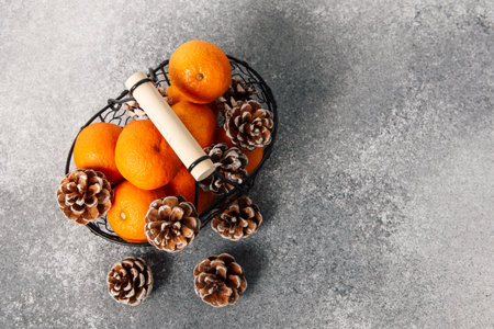 A wire basket holds bright oranges and charming pine cones arranged neatly. The background is a smooth gray surface creating a simple and clean display.の写真素材