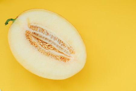 A melon is cut in half exposing its seeds and soft flesh. The yellow background highlights the details of the melon. The setting offers a simple yet vibrant display of fruit and color.の写真素材