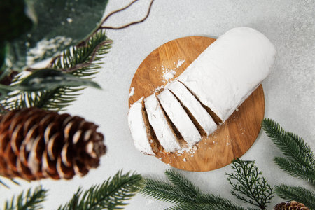 stollen cake is sliced and covered in powder. The bread is placed on a wooden board. Pine branches...