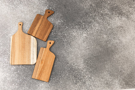 Three wooden cutting boards are arranged on a gray surface. They vary in size and shape. These...