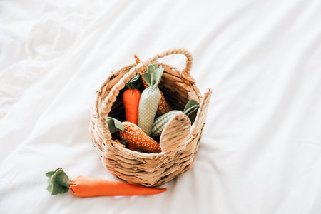 A woven basket holds several colorful toy carrots resting on a white blanket. The toys are made of fabric and show various patterns. The setting appears bright and inviting in a room.の写真素材