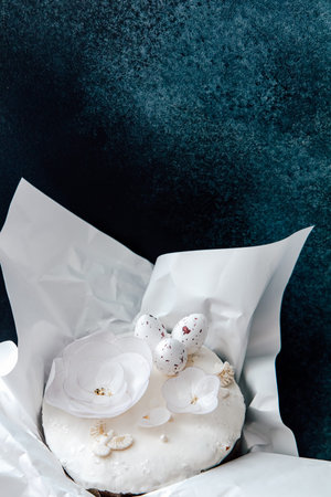 A cake is decorated with white flowers and small ornaments. It is wrapped in white paper and set...