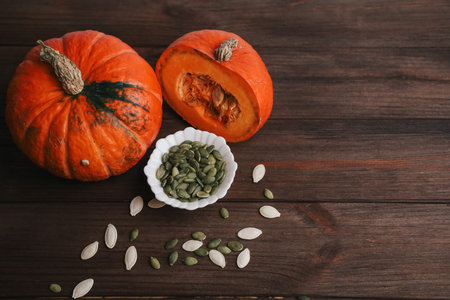 Two pumpkin halves are placed next to a small dish of pumpkin seeds on a wooden table. This scene captures the essence of autumn and the approaching Halloween season.