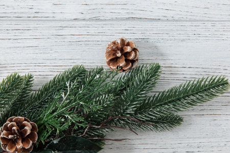 Pinecones sit among green evergreen branches on a light wooden table. The scene shows a simple winter decoration with natural elements.
