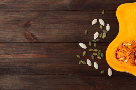 A cut pumpkin rests on a dark wooden surface with seeds lying next to it. This scene shows a kitchen activity, preparing for fall recipes. The focus is on the natural elements.