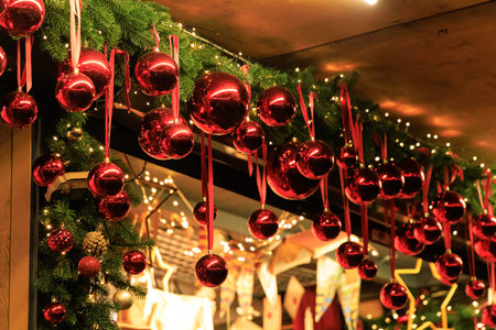Red ornaments are hung with ribbons along a festive display at a market. Lights twinkle in the background capturing the holiday spirit and activity.