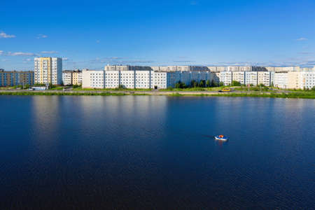 Nadym, RUSSIA-JULY 03, 2020: View of city multi-storey buildings and a boat on a lake on a summer day in the North of Western Siberiaのeditorial素材