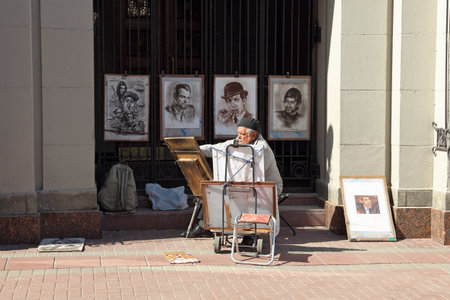 MOSCOW, RUSSIA-APRIL 30, 2017: An elderly artist paints portraits of famous politicians and musicians for tourists on Arbat Street in the Russian capitalのeditorial素材