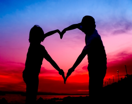 silhouette young couple making heart shape with arms on beach at sunsetの写真素材