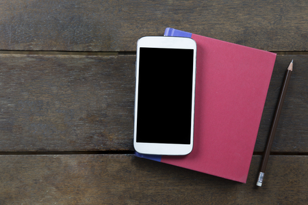 Empty screen mobile on red cover book and pencil on old wooden background topview flatlay clippingpath at screen copyspaceの写真素材