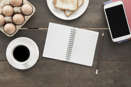 Black coffee note book toast eggs and mobile on red cover book on old wooden table background concept idea topview flatlay with clipping path at screenの写真素材