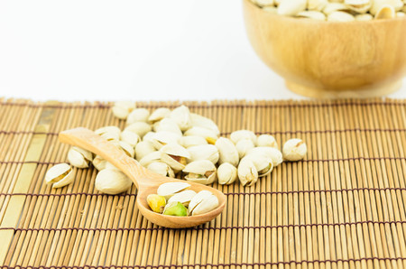 Pistachio nuts on wooden spoon with white backgroundの写真素材