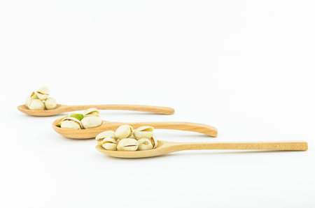 Pistachio nuts on wooden spoon with white  backgroundの写真素材