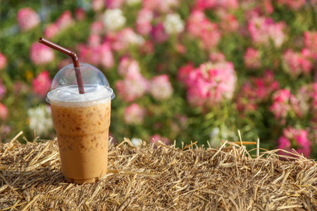 A cup of iced coffee on rice straw bales with flower  background.