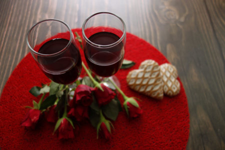 Red wine glasses, roses and heart shaped cookies on wooden background, Valentine`s Day conceptの写真素材