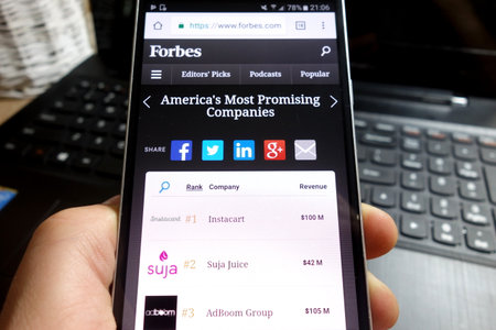 KONSKIE, POLAND - MAY 07, 2018: Man holding his smartphone and scrolling the ranking of America`s most promising companies on the official Forbes magazine websiteのeditorial素材