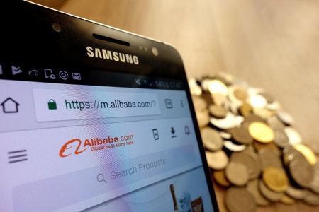 KONSKIE, POLAND - MAY 14, 2018: Alibaba website is displayed on smartphone and stack of coinsのeditorial素材