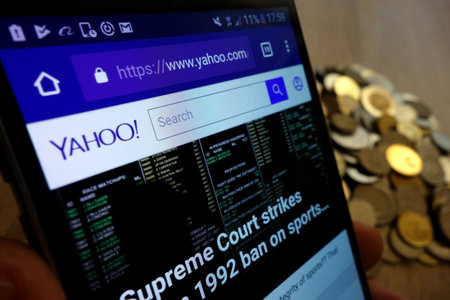 KONSKIE, POLAND - MAY 14, 2018: Yahoo website displayed on smartphone and stack of coinsのeditorial素材