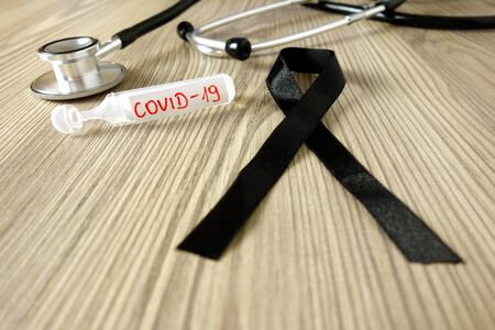 Mourning ribbon ampoule with text Covid-19 and stethoscope on doctor office desk. Coronavirus death victim conceptの写真素材