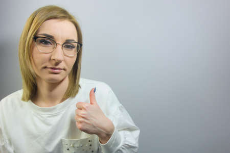Young beautiful blond woman wearing casual shirt and glasses on isolated background doing happy thumbs up sign. Approving expression, success conceptの写真素材