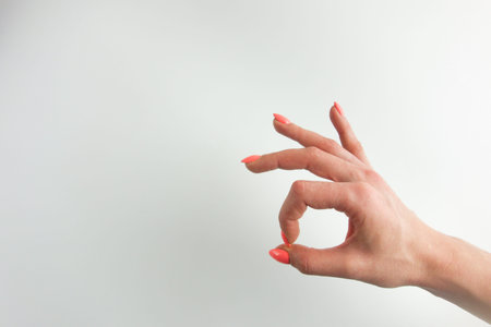 Woman's hand with pastel orange fingernails making ok gesture. White background, copy space for your designの写真素材