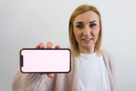 Attractive young blond caucasian woman showing mobile phone mockup. Copy space for your text and designの写真素材
