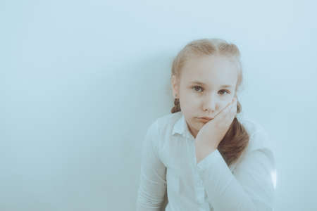 Portrait of sad little Caucasian girl standing near wall. Worry, unhapiness, problems, outcast, children drama concept. Copy space for designの写真素材