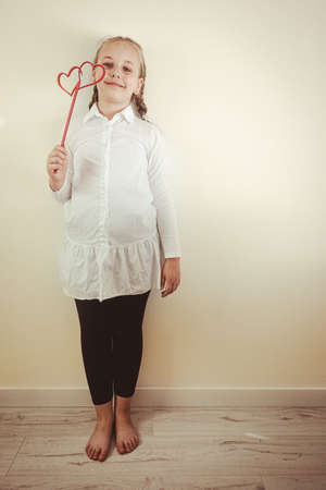 Portrait of young smiling beautiful blonde girl holding heart shaped decoration. Happy childhood, love, positive feeling and emotion concept. Copy space for designの写真素材