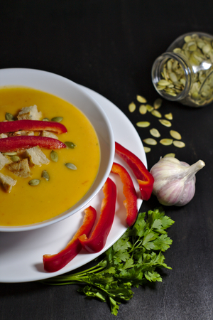 pumpkin soup with paprika, seeds, garlic, rusks and greens on dark backgroundの写真素材