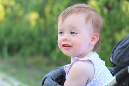 little, beautiful, smiling, cute redhead baby in a pram out-of-doors in a sleeveless shirt