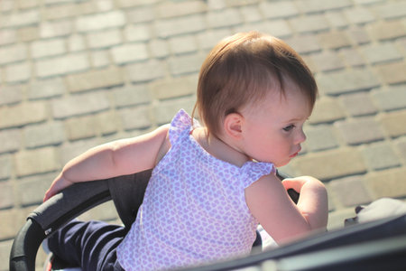 little, beautiful, smiling, cute redhead baby in a sleeveless shirt in a pram out-of-doors drops...