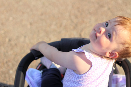 little, beautiful, smiling, cute baby in a sleeveless shirt in a pram out-of-doors drops hands down and looking backの写真素材